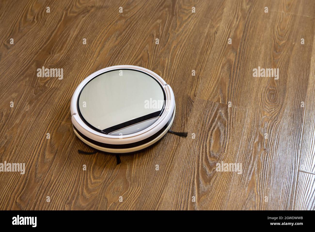 Aspiradora de robot inalámbrica redonda blanca sobre suelo laminado marrón.  Concepto Limpieza diaria en casa Fotografía de stock - Alamy