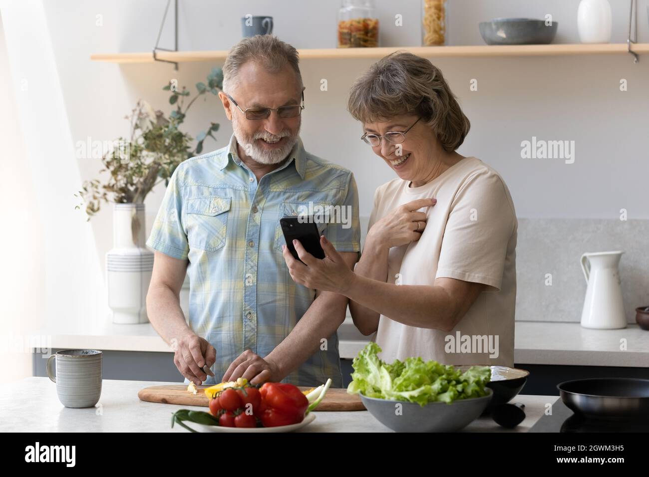 Feliz pareja de edad cocinar, utilizando aplicaciones de telefonía móvil. Foto de stock