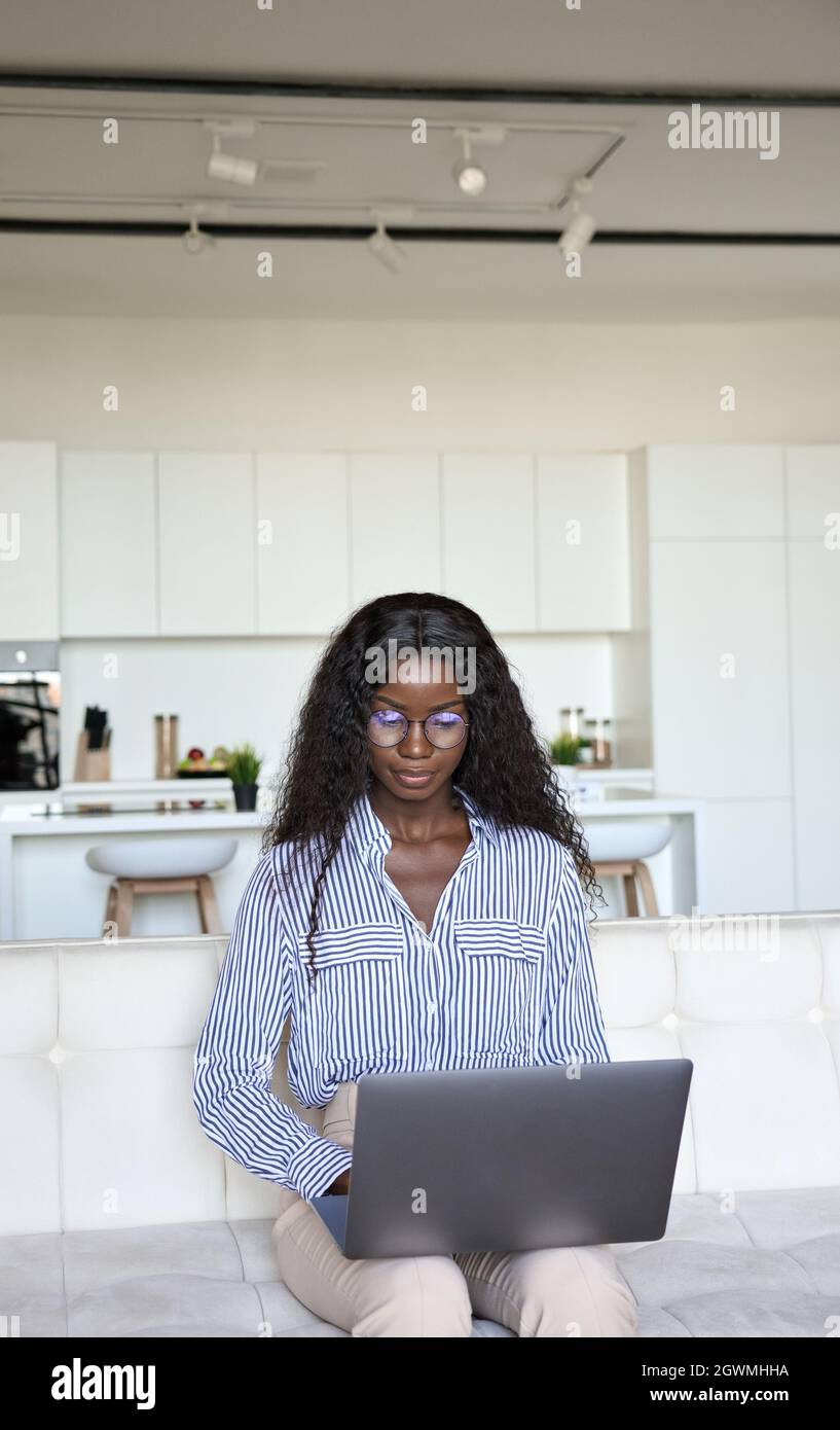 Joven inteligente mixta raza negra hembra sentada escribiendo con el portátil. Foto de stock