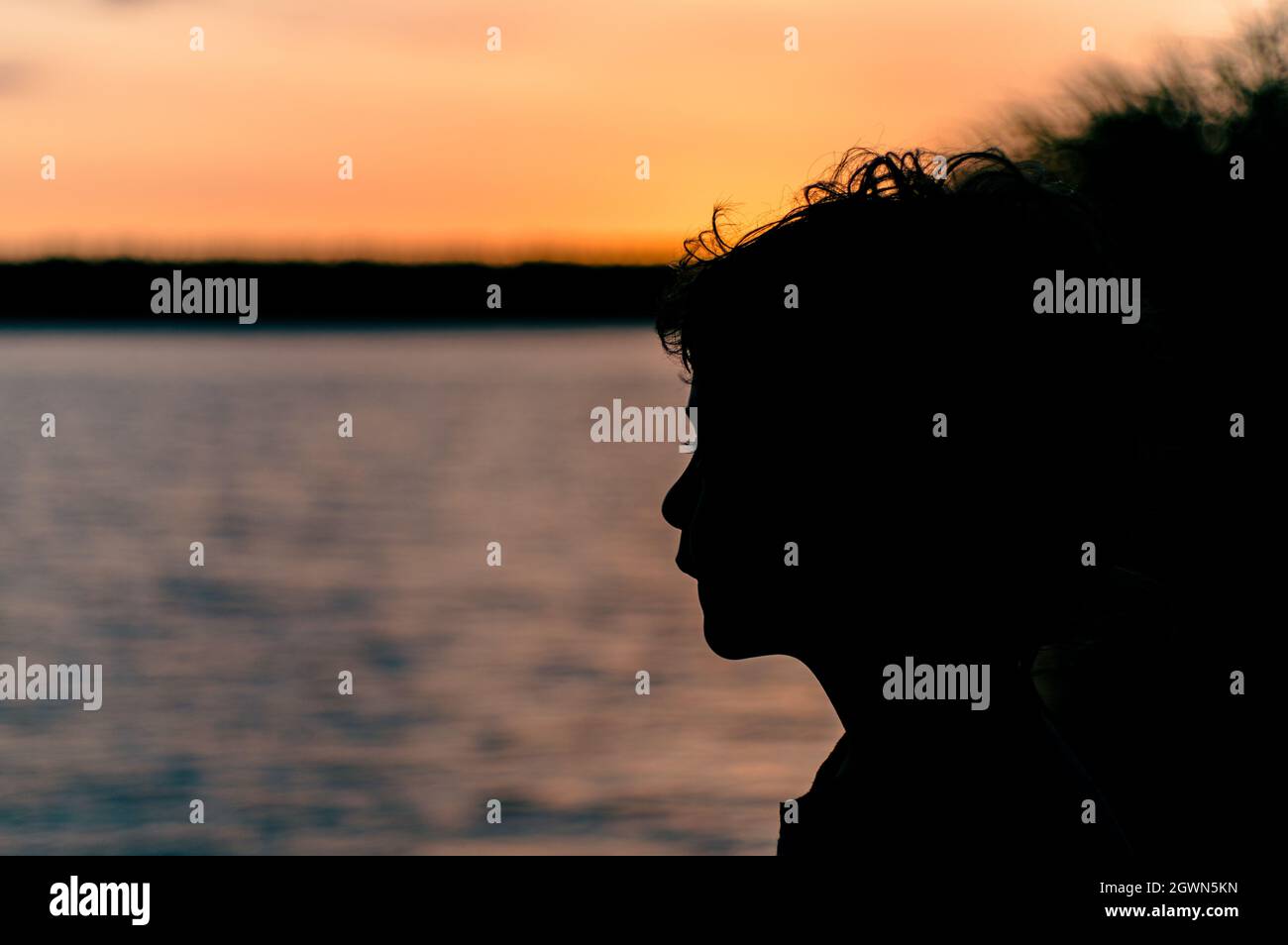 Primer plano Retrato de Silhouette Boy contra el lago durante la puesta de sol Foto de stock