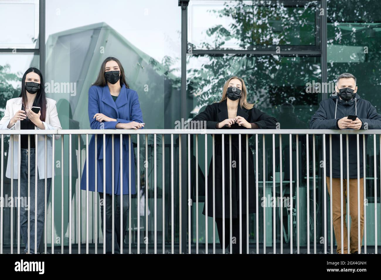 Lo nuevo es el concepto normal, la distancia social, el brote de coronavirus. Jóvenes milenarios posando con máscaras protectoras negras y teléfonos celulares en el ar urbano Foto de stock