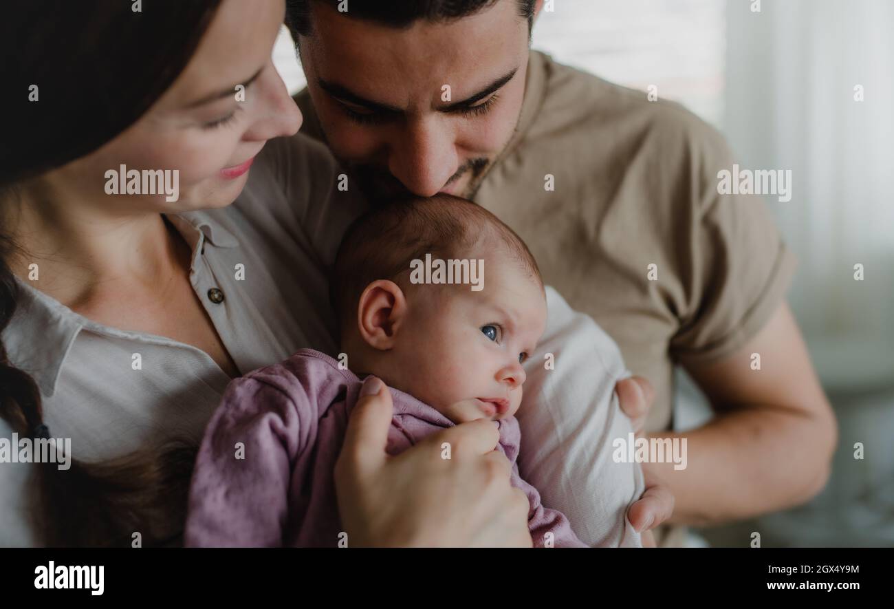 Cerca de los padres jóvenes sosteniendo y besando a su bebé recién nacido en casa Foto de stock