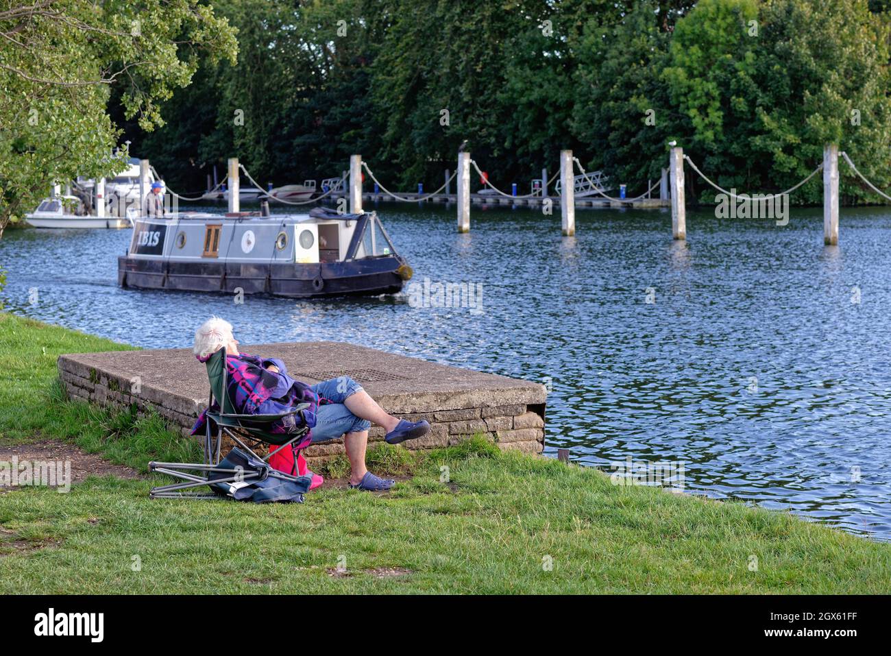 Una anciana durmiendo en una silla de lona junto al río Támesis en Shepperton con un barco estrecho que pasa al fondo, Surrey Inglaterra Reino Unido Foto de stock