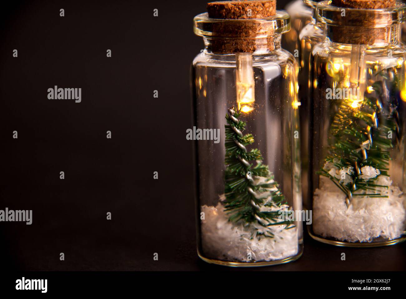 Primer plano de luces brillantes decoración de tarros de vidrio con corchos en el interior que hay pequeños árboles verdes de Navidad en la nieve artificial. Vacaciones Nueva Yea Foto de stock