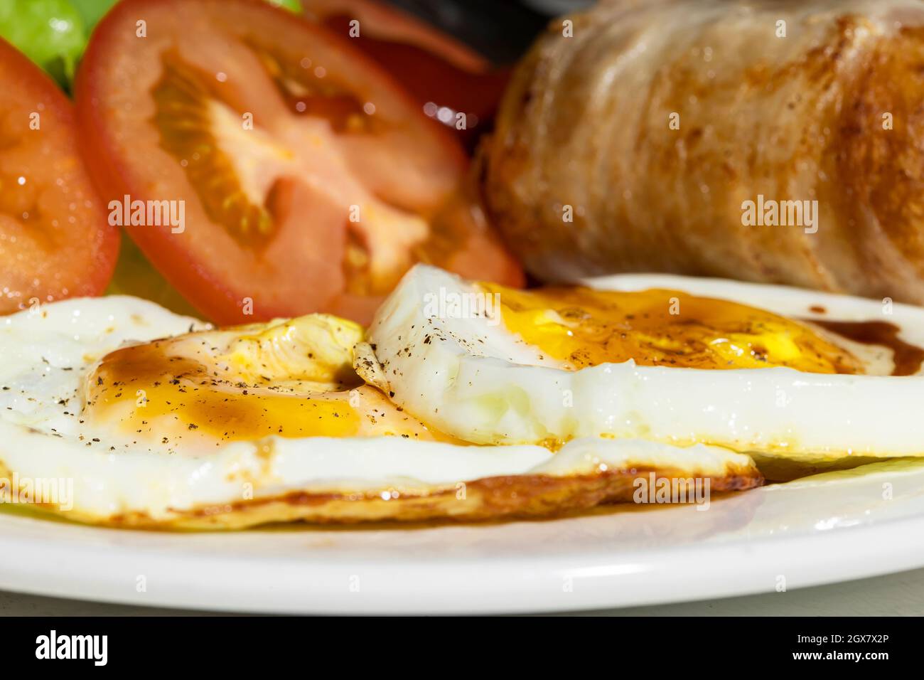 En primer lugar se colocaron huevos fritos, salchichas y tomate en un plato blanco para el desayuno. Foto de stock