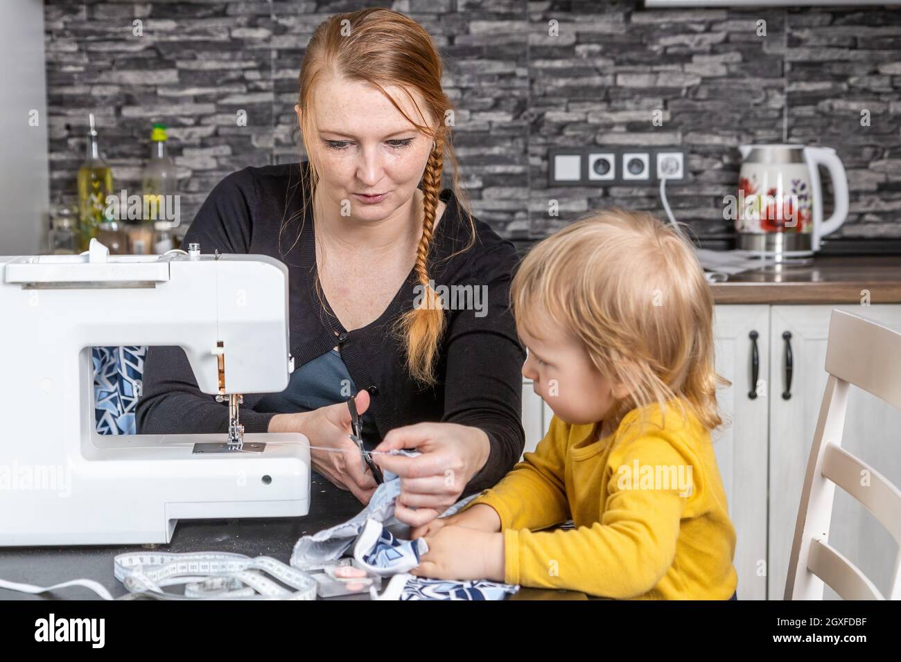 https://c8.alamy.com/compes/2gxfdbf/nino-observa-a-su-joven-madre-ella-esta-cortando-la-tela-horizontalmente-2gxfdbf.jpg