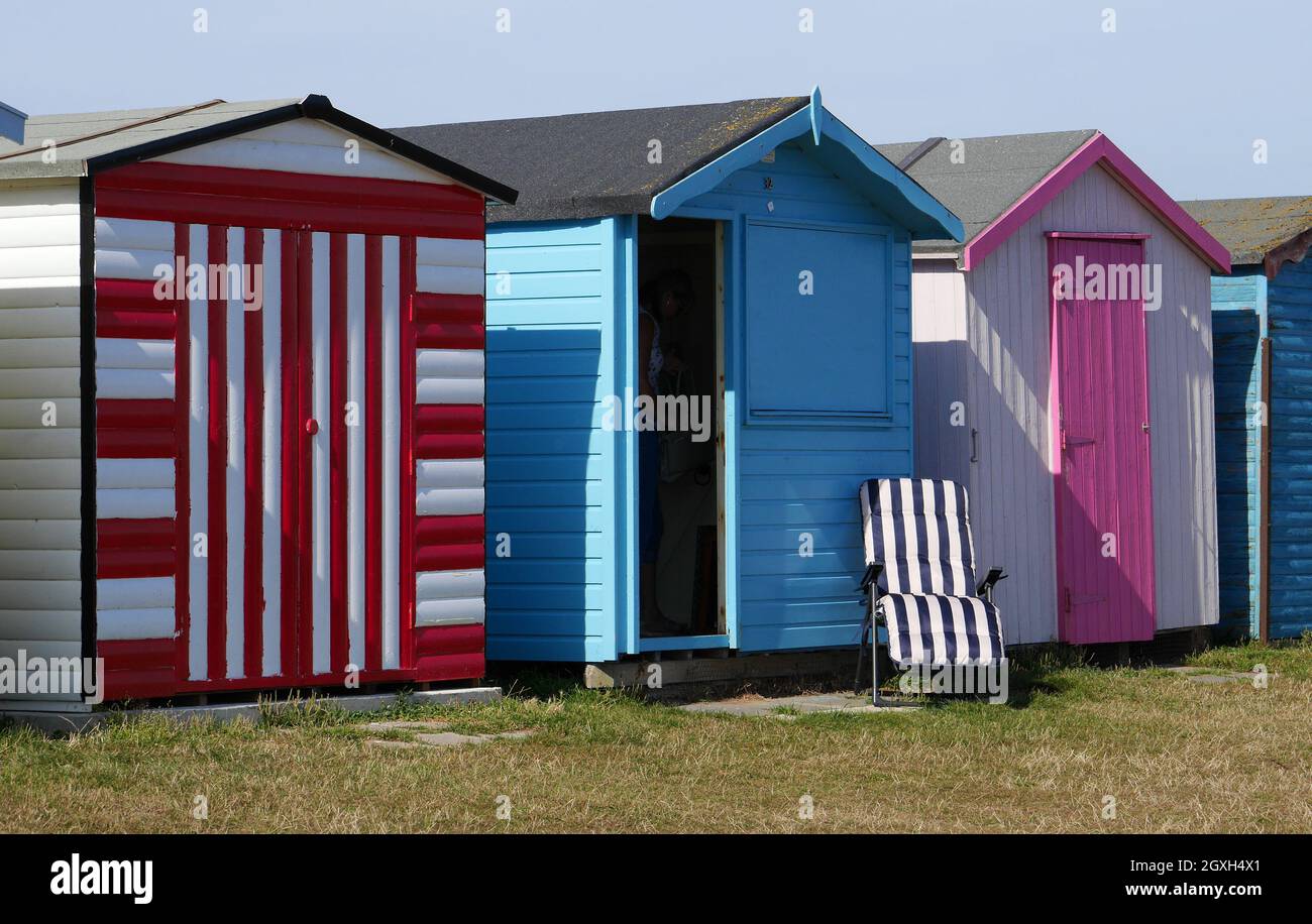 Coloridas cabañas en la playa junto al mar con una tumbona desnuda vacía, Dovercourt Bay, Harwich, Essex, Inglaterra, REINO UNIDO Foto de stock