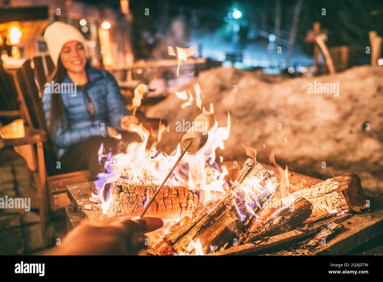 Vacaciones de invierno estación de esquí mujer tostar malvaviscos en barbacoa fogata después de esquiar diversión actividad de ocio con amigos. Un par de bastón de asar se adhieren Foto de stock