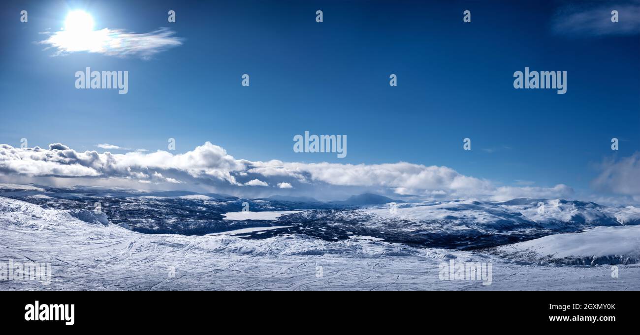 Vista panorámica muy panorámica de las montañas escandinavas, pista de esquí con muchos rastros. No hay gente todavía, día soleado, mucha nieve y cielos azules con suave clo Foto de stock