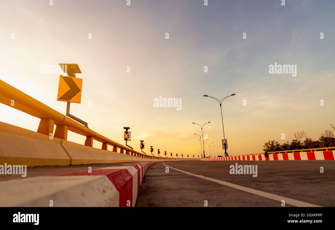 Carretera curva de hormigón con señal de tráfico curva y señal de stop roja-blanca prohibida. Curva de carretera al lado del mar a la puesta del sol. Energía del panel solar en amarillo Foto de stock