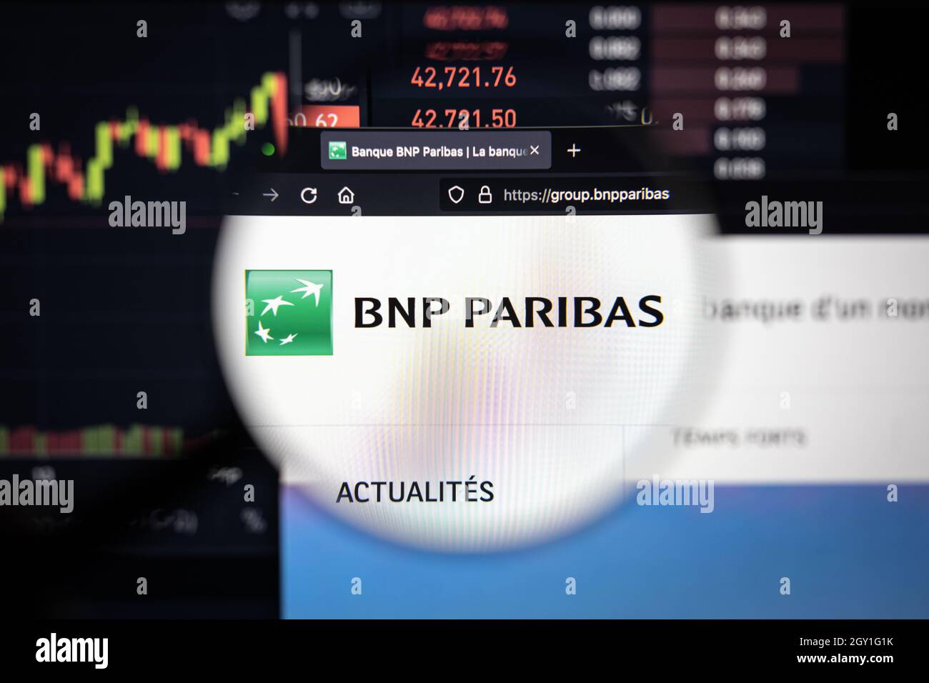 BNP Paribas logotipo de la empresa en un sitio web con la borrosos evolución del mercado de valores en el fondo, visto en una pantalla de ordenador a través de una lupa Foto de stock