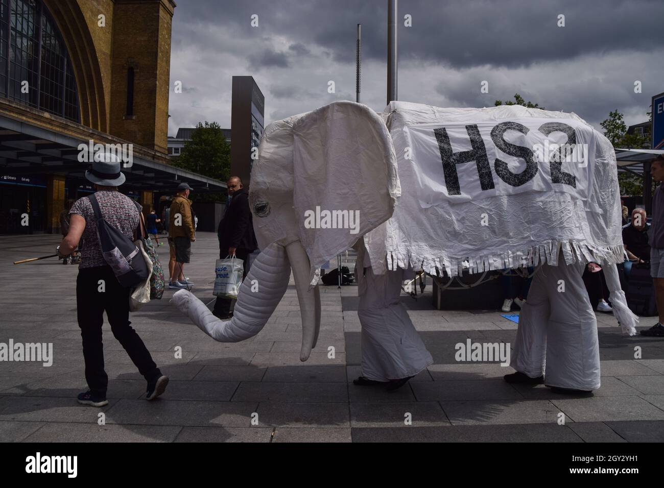 Londres, Reino Unido. 5th de agosto de 2021. Los manifestantes que llevan un traje de elefante blanco 'HS2' son conducidos fuera de la estación de tren por un manifestante. Los activistas se reunieron fuera de la estación de King's Cross en protesta contra el nuevo sistema ferroviario High Speed 2 (HS2), que los ecologistas dicen que será 'ecológicamente devastador' y costará a los contribuyentes £170 mil millones. Foto de stock