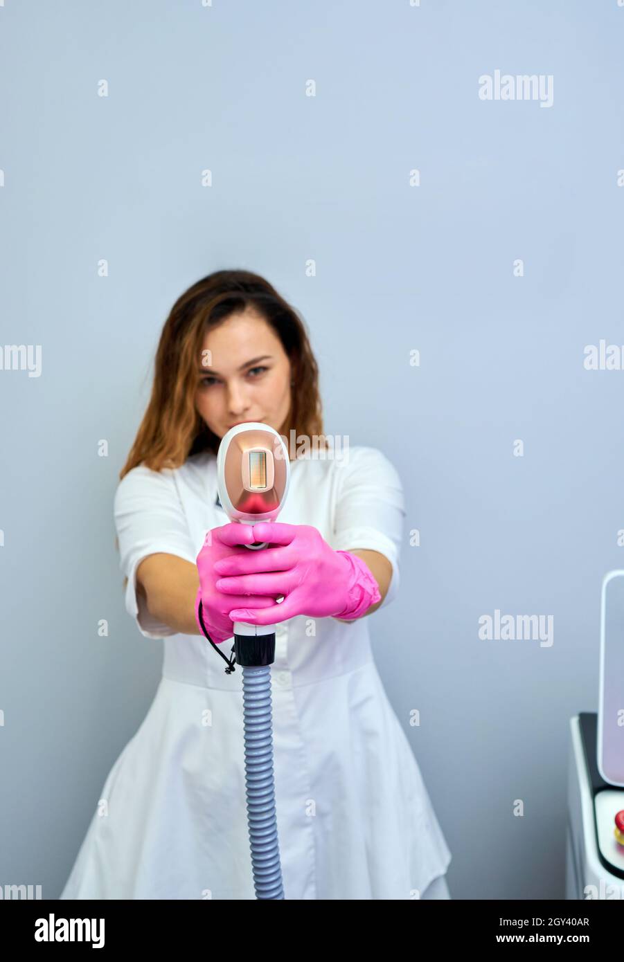 Una mujer sintoniza una máquina de depilación láser. Ella sostiene una  parte de trabajo de la depiladora en sus manos y posará para hacer una  foto. Está situado en un moderno bea