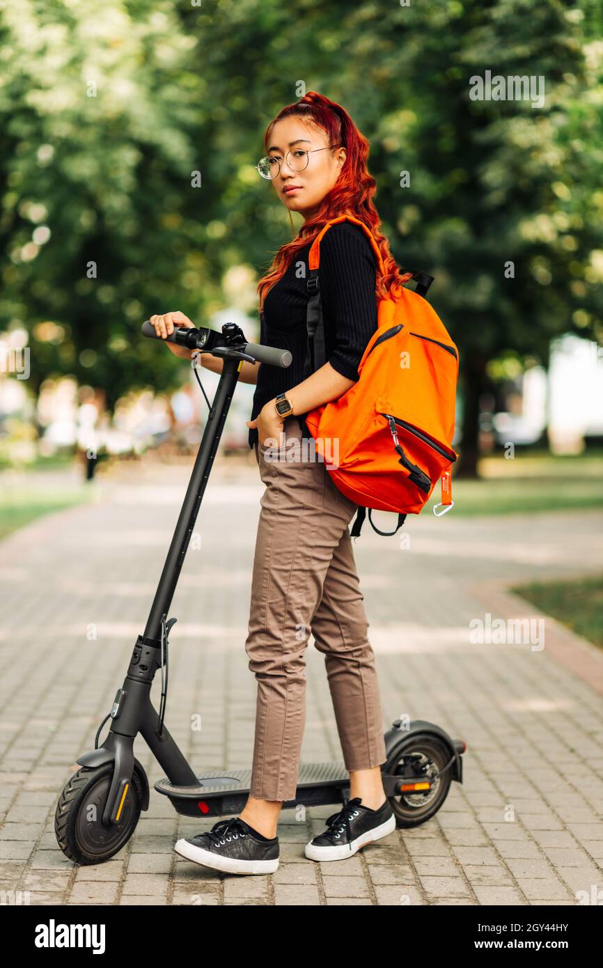 Joven hermosa estudiante asiática, con una mochila, camina en el parque con  un scooter eléctrico, en el verano en la calle Fotografía de stock - Alamy
