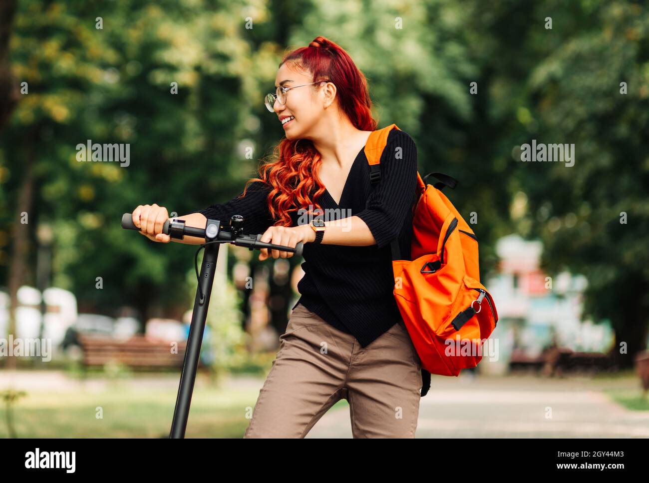 Joven hermosa estudiante asiática, con una mochila, camina en el parque con  un scooter eléctrico, en el verano en la calle Fotografía de stock - Alamy