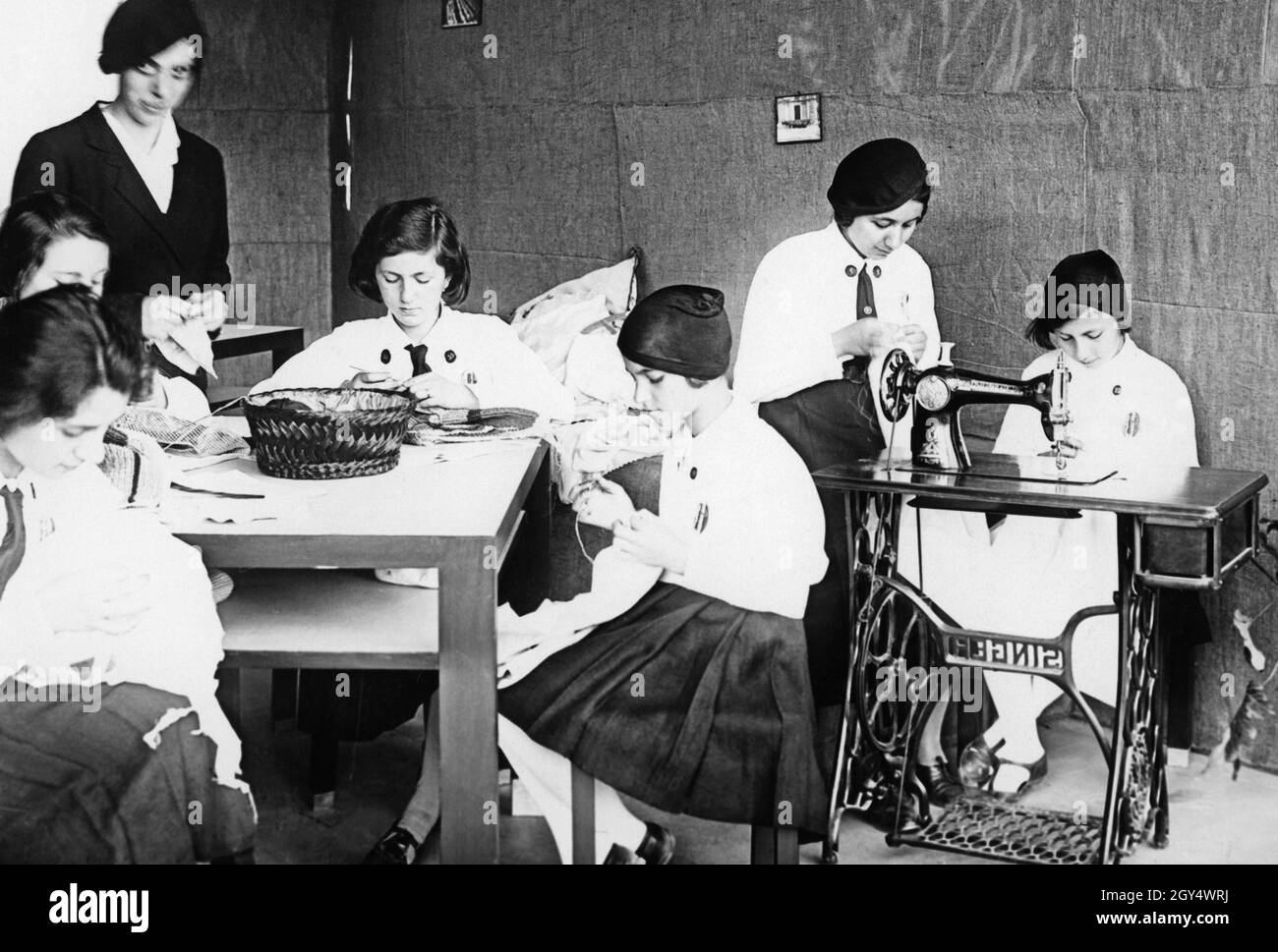 Las niñas aprenden a embroidarse y coser en una escuela italiana bajo la supervisión de un profesor (izquierda). Un estudiante se sienta en una máquina de coser Singer. La foto fue tomada en 1937. [traducción automática] Foto de stock