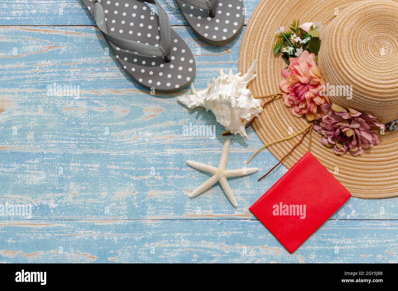 Flat Lay verano accesorios de playa de señora floreada sombrero de paja,  chanclas y pasaporte rojo con conchas y estrellas de mar sobre fondo de  madera azul. Summe Fotografía de stock -