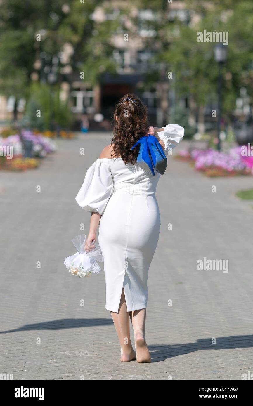 Una novia sin zapatos de vestido blanco con un ramo de flores y zapatos  azules en sus manos está caminando por la ciudad Fotografía de stock - Alamy