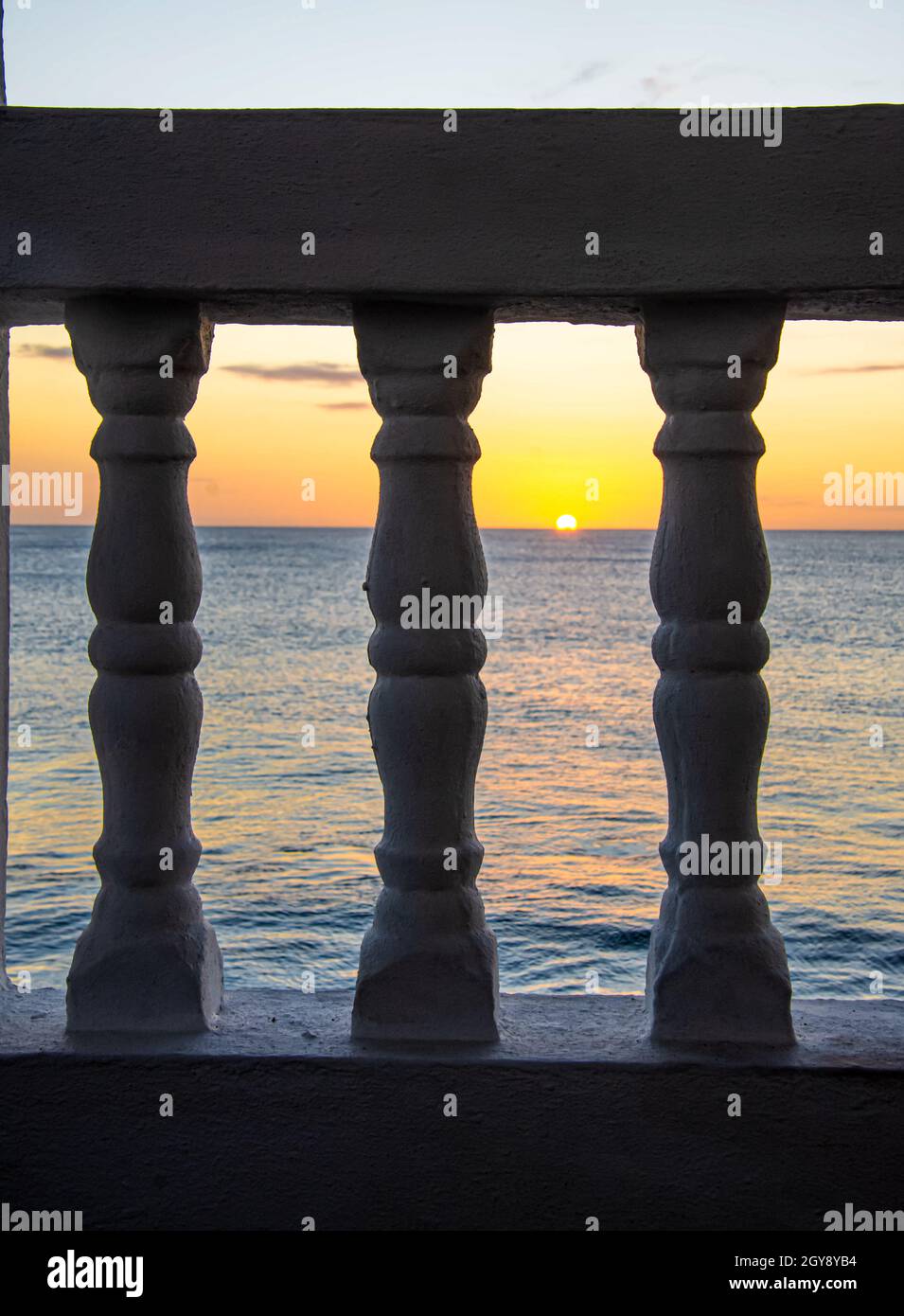 La puesta de sol a través de balaustradas en un balcón frente a la playa. Rincón, Puerto Rico. Foto de stock