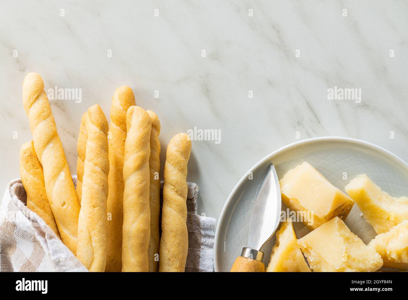 Palos de grissini y queso parmesano. Comida tradicional italiana sobre mesa blanca. Vista superior. Foto de stock