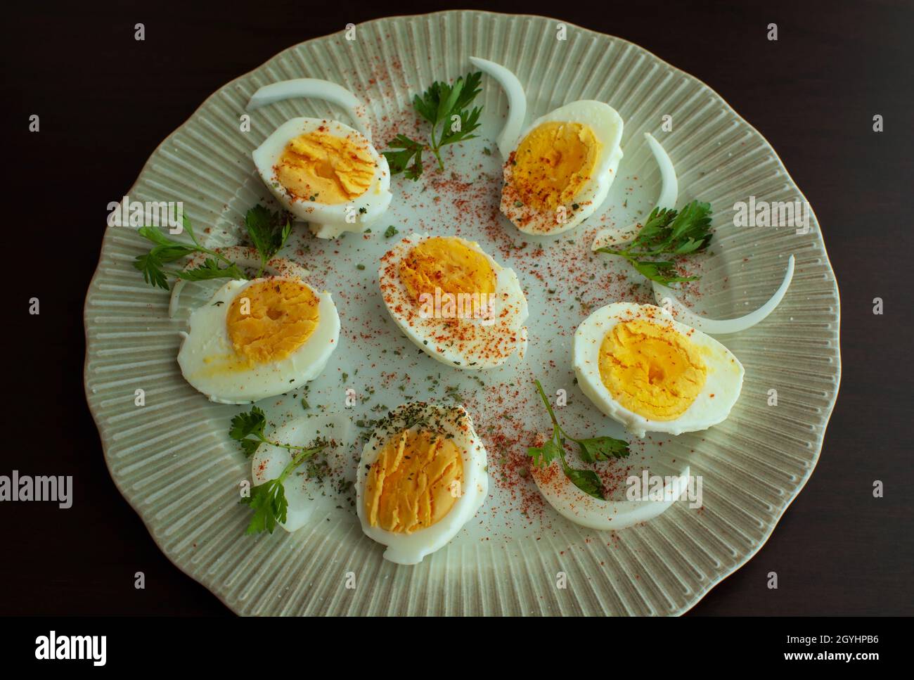 Huevo cocido en un plato decorado con hojas de perejil, cebollas y especias. Foto de stock