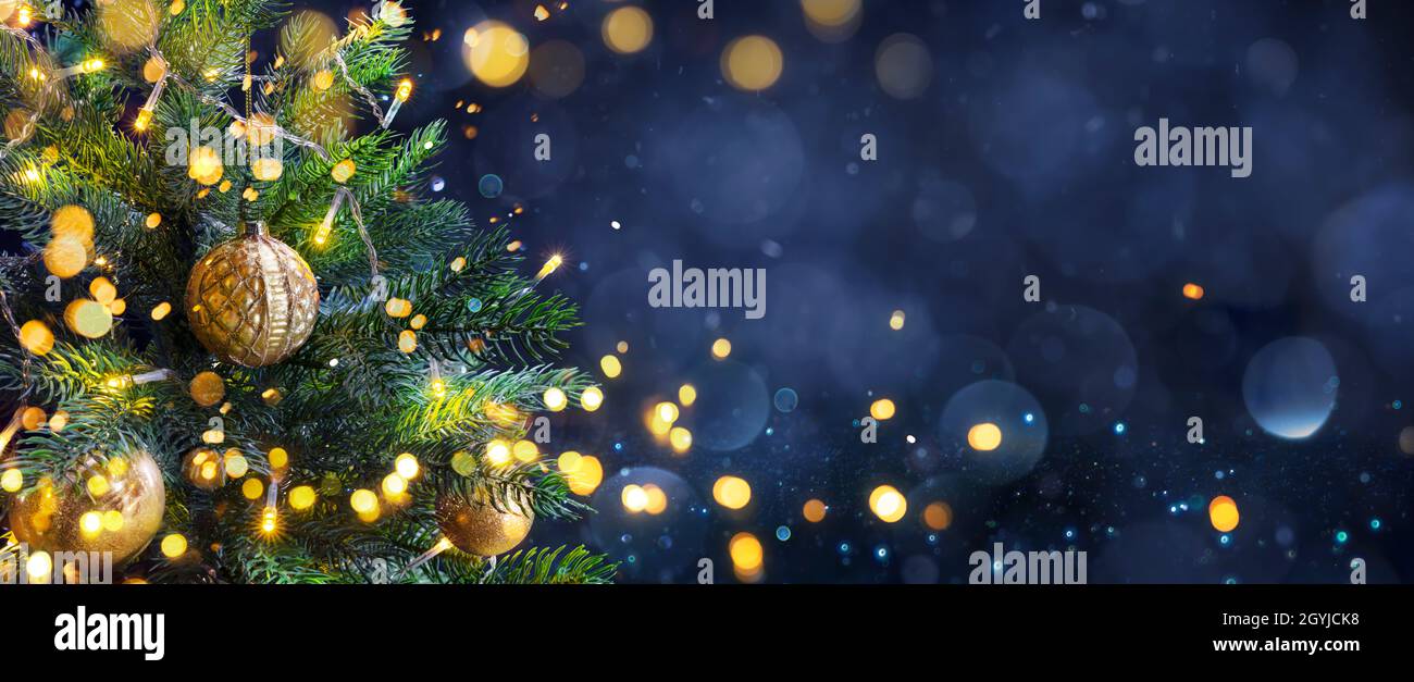 Árbol de Navidad en Noche Azul - Bolas de Oro en ramas de abeto con luces desempleadas en fondo abstracto Foto de stock