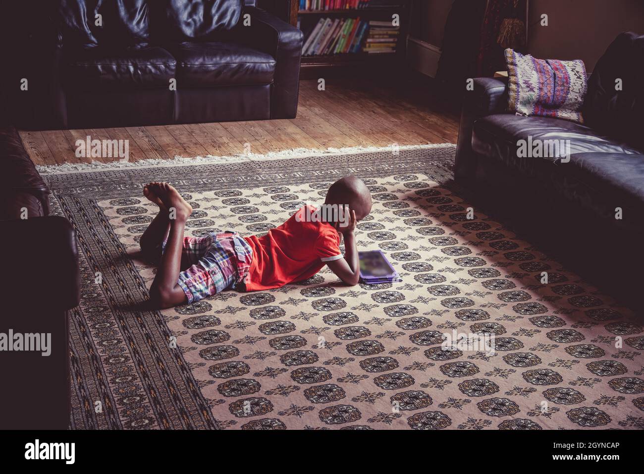 Joven negro, étnicamente diverso, niño usando una tableta en un ambiente relajado hogar Foto de stock