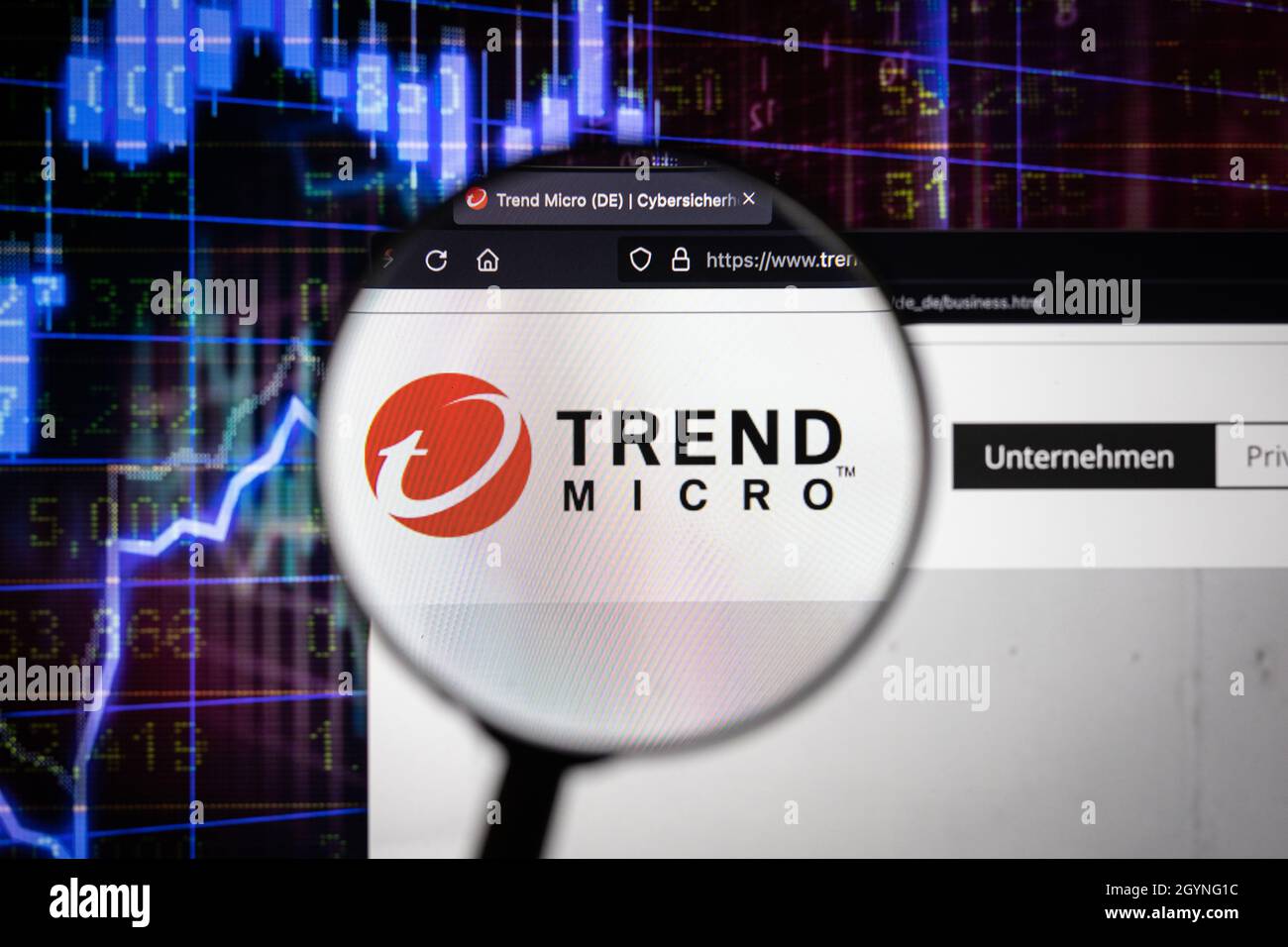 Logotipo de la empresa Trend Micro en un sitio web con una evolución borrosa del mercado de valores en segundo plano, visto en una pantalla de ordenador a través de una lupa Foto de stock