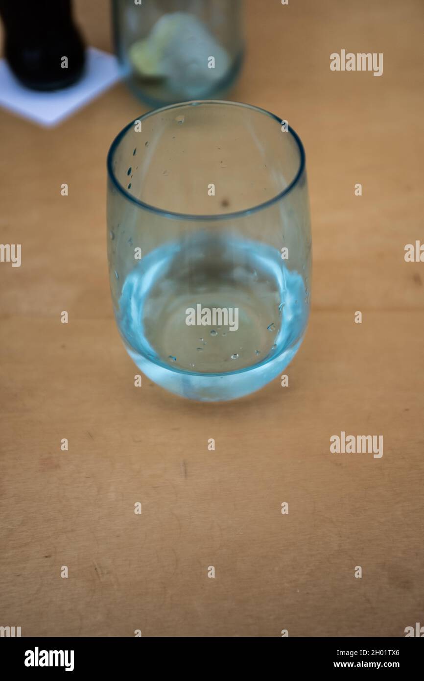 Vaso de beber azul transparente con agua fresca y algunas gotas sobre él en una mesa de madera cerca de quieto Foto de stock