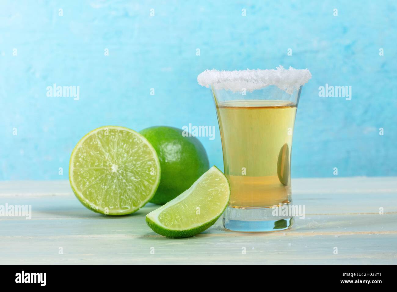 Tequila rodó con rodajas de lima, una bebida mexicana sobre un fondo azul vibrante, con un borde de sal, vista lateral Foto de stock