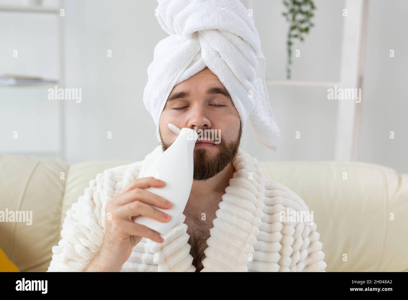 Hombre barbudo con una toalla en la cabeza aplicando crema de loción corporal. El tipo sonríe cuando huele loción a mano. Spa, cuidado corporal y de la piel para el