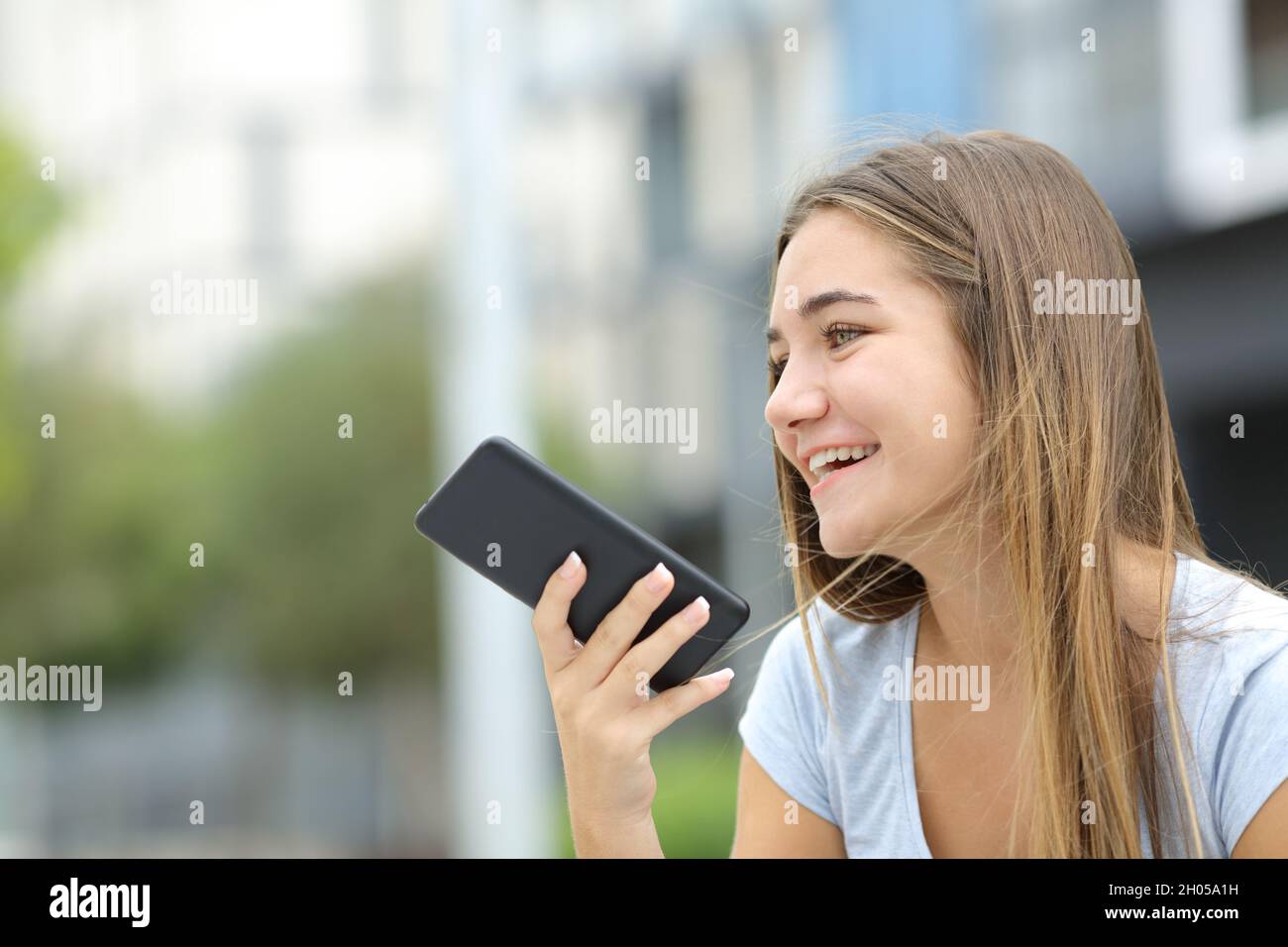Feliz adolescente utilizando el reconocimiento de voz en el teléfono inteligente en la calle Foto de stock