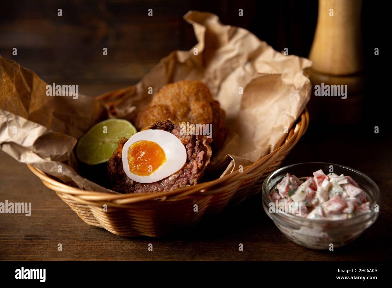 Porción de huevo escocés y salsa pico de gallo servido en papel de сraft y  cesta de mimbre. Comida frita de pub tirada en el interior de un bar  Fotografía de stock -