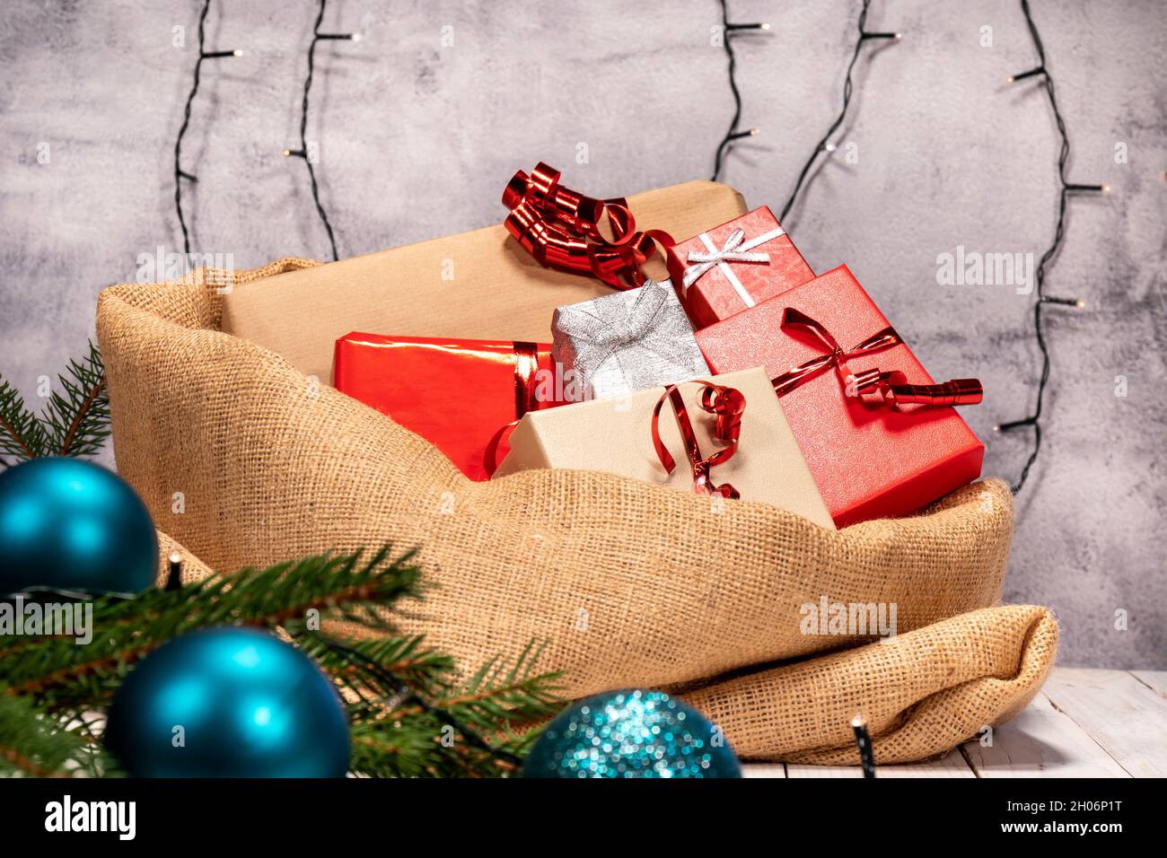 Saco de yute lleno de regalos de Navidad sobre una mesa de madera blanca.  Regalos con papel rojo, marrón y plata con cinta roja, decoraciones  navideñas alrededor Fotografía de stock - Alamy