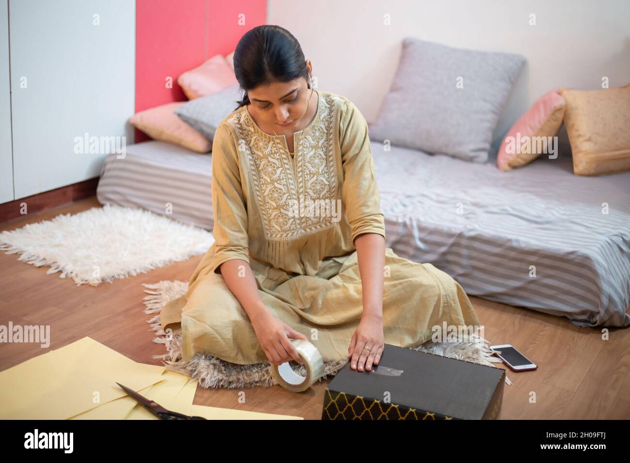 Mujer joven del negocio indio que embala ropa nueva o vestidos para vender  la tienda de la tela, dueño en línea pequeño de la ropa del inicio,  preparando productos para el envío