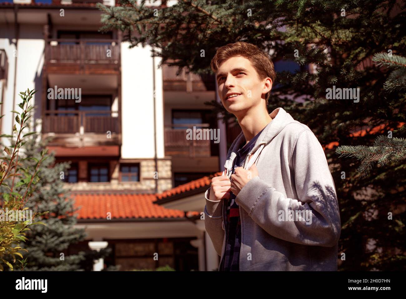 Joven hombre guapo de pie cerca de pino, bonita casa en la ciudad  Fotografía de stock - Alamy
