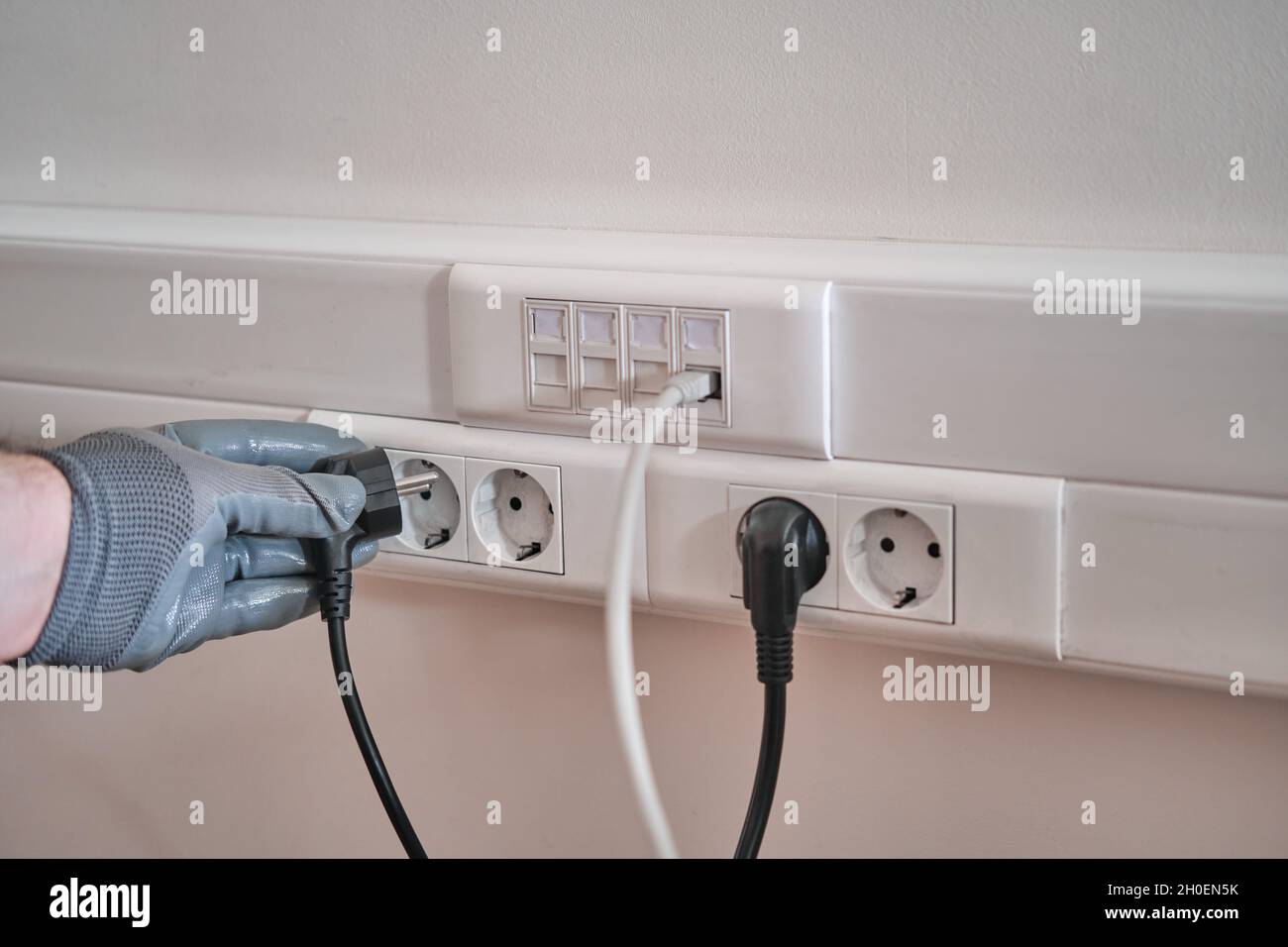Conexión a la red eléctrica En la oficina, una mano enguantada sujeta el  cable para conectarlo a la toma de corriente Fotografía de stock - Alamy