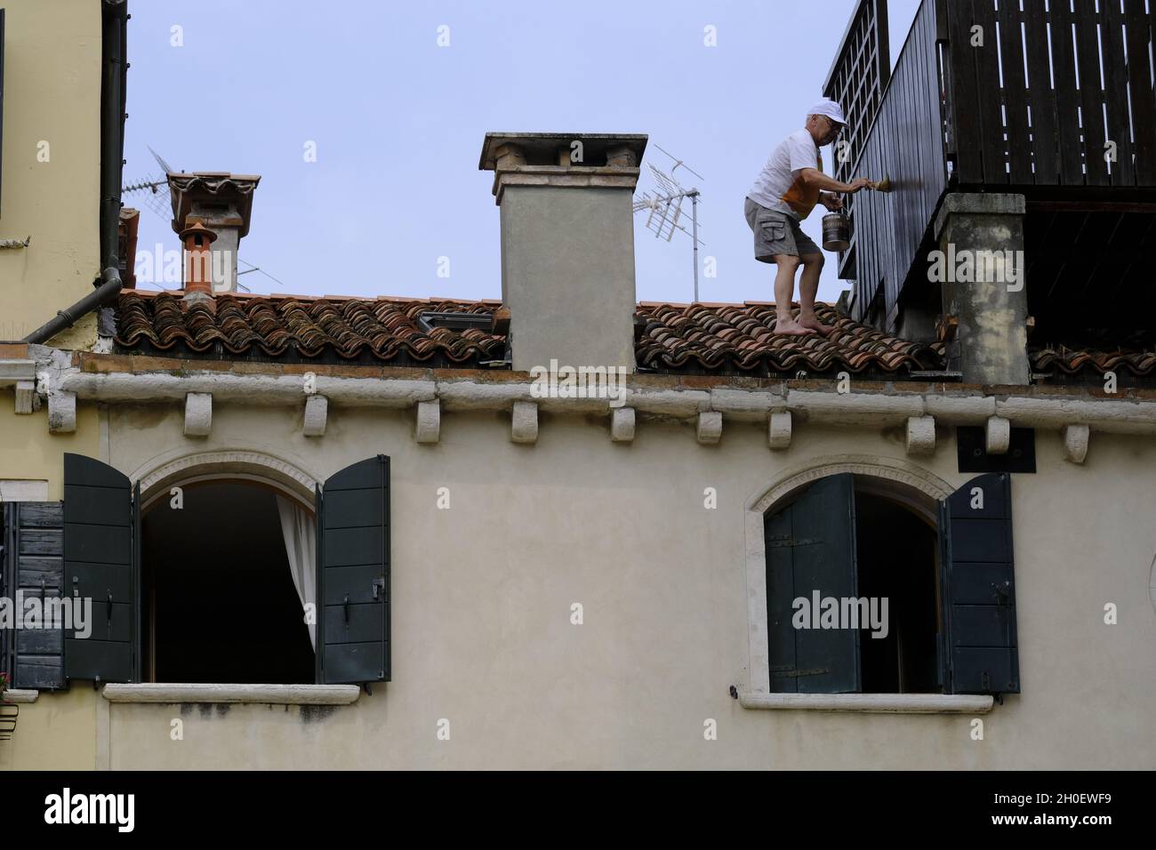 Un hombre pinta su terraza en el techo de una casa en Venecia, Italia, 18 de junio de 2021.(MVS) Foto de stock