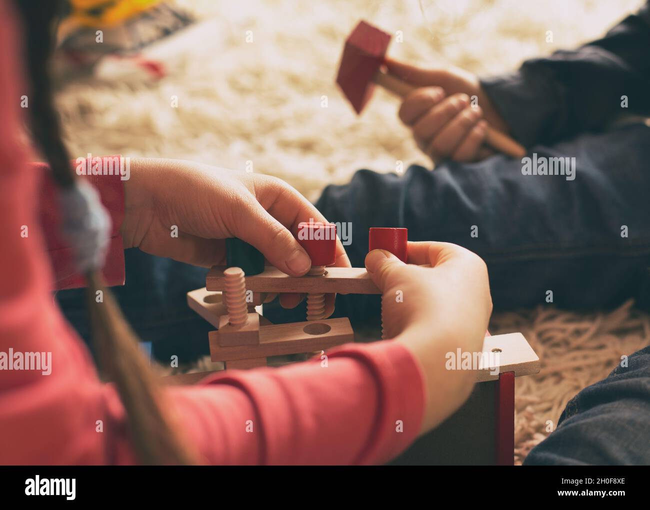 Niño y niña jugando con juguetes de madera en la alfombra. Primer plano de las manos que practican habilidades motoras con herramientas de trabajo Foto de stock