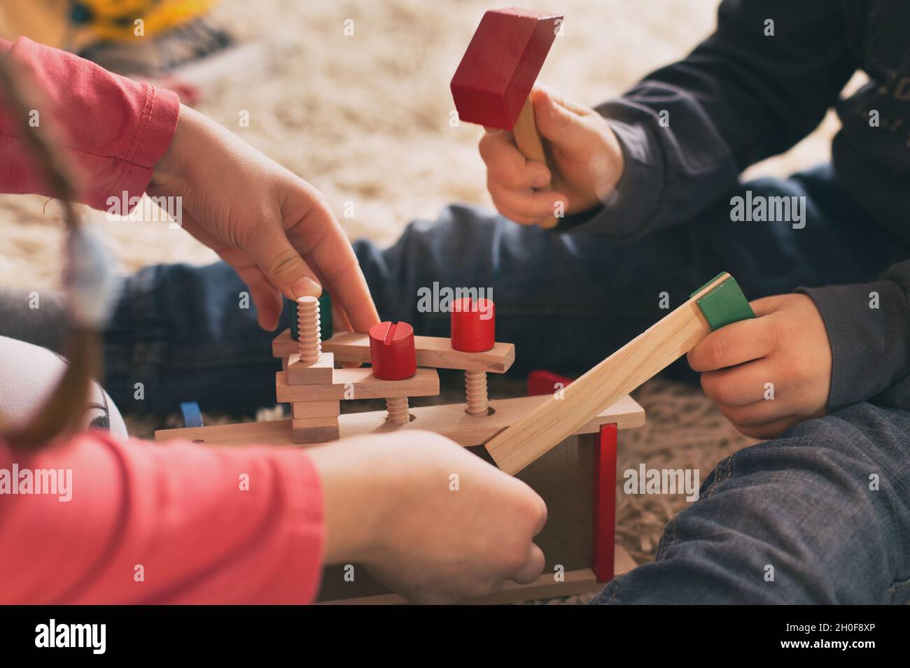 Niño y niña jugando con juguetes de madera en la alfombra. Primer plano de las manos que practican habilidades motoras con herramientas de trabajo Foto de stock