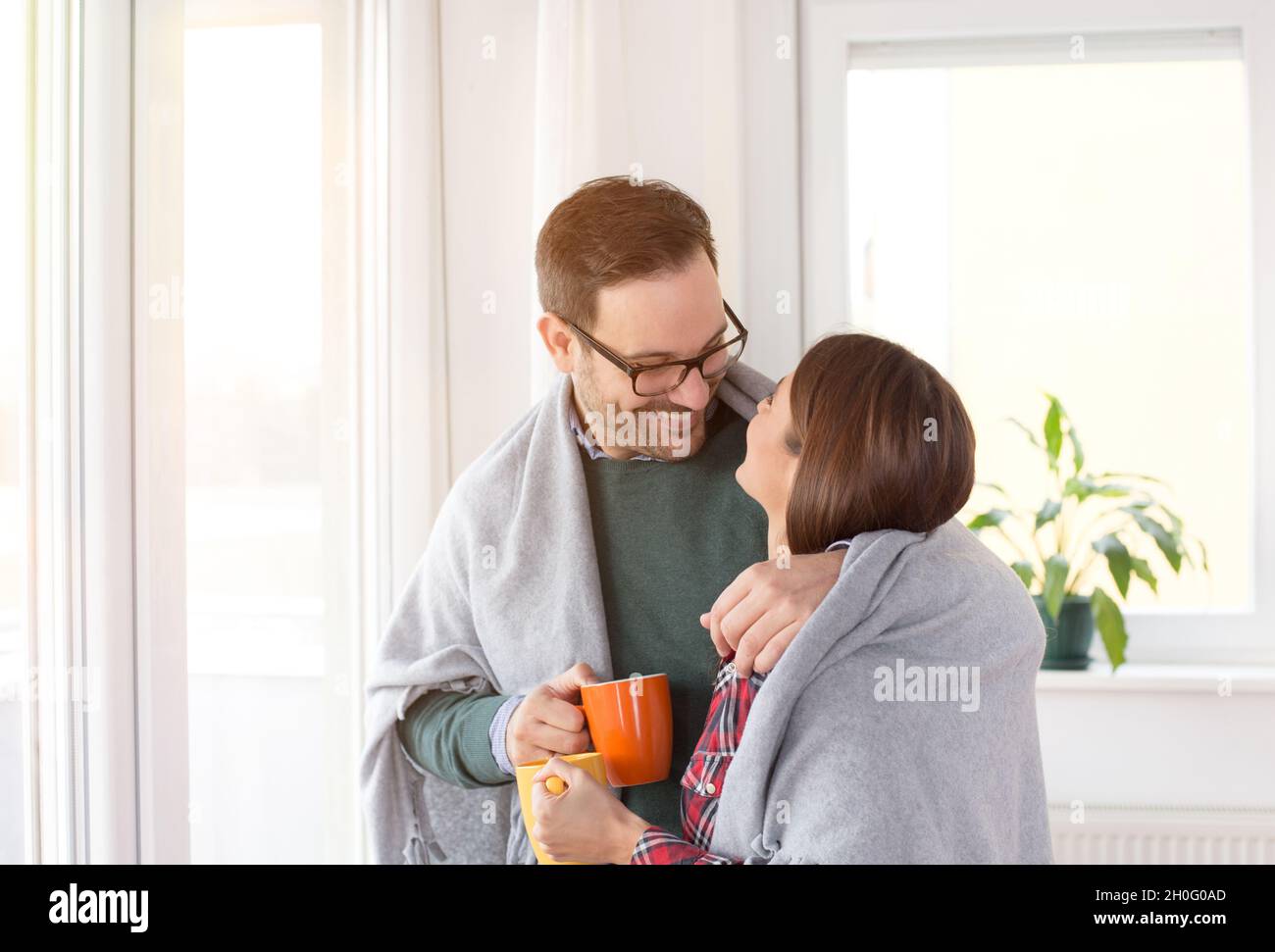 Feliz pareja joven calentándose unos a otros bajo manta en abrazo al lado  de las ventanas en casa Fotografía de stock - Alamy