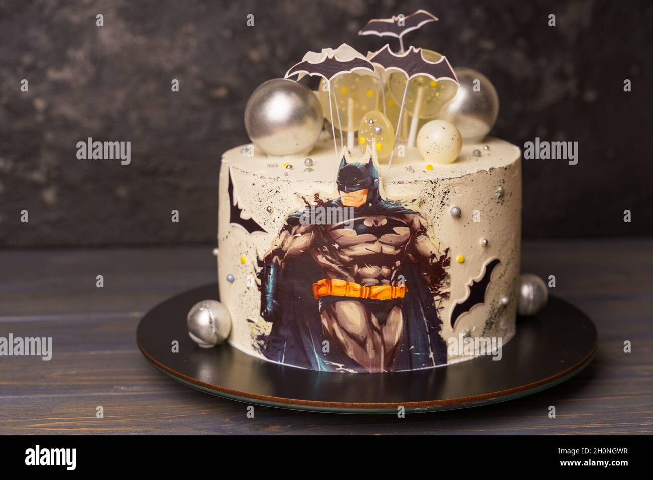 Pastel para una fiesta infantil con la imagen de Batman, decorado con  piruletas, bolas de chocolate, murciélagos. Pastel de cumpleaños con un  héroe cómico en un oscuro backg Fotografía de stock -