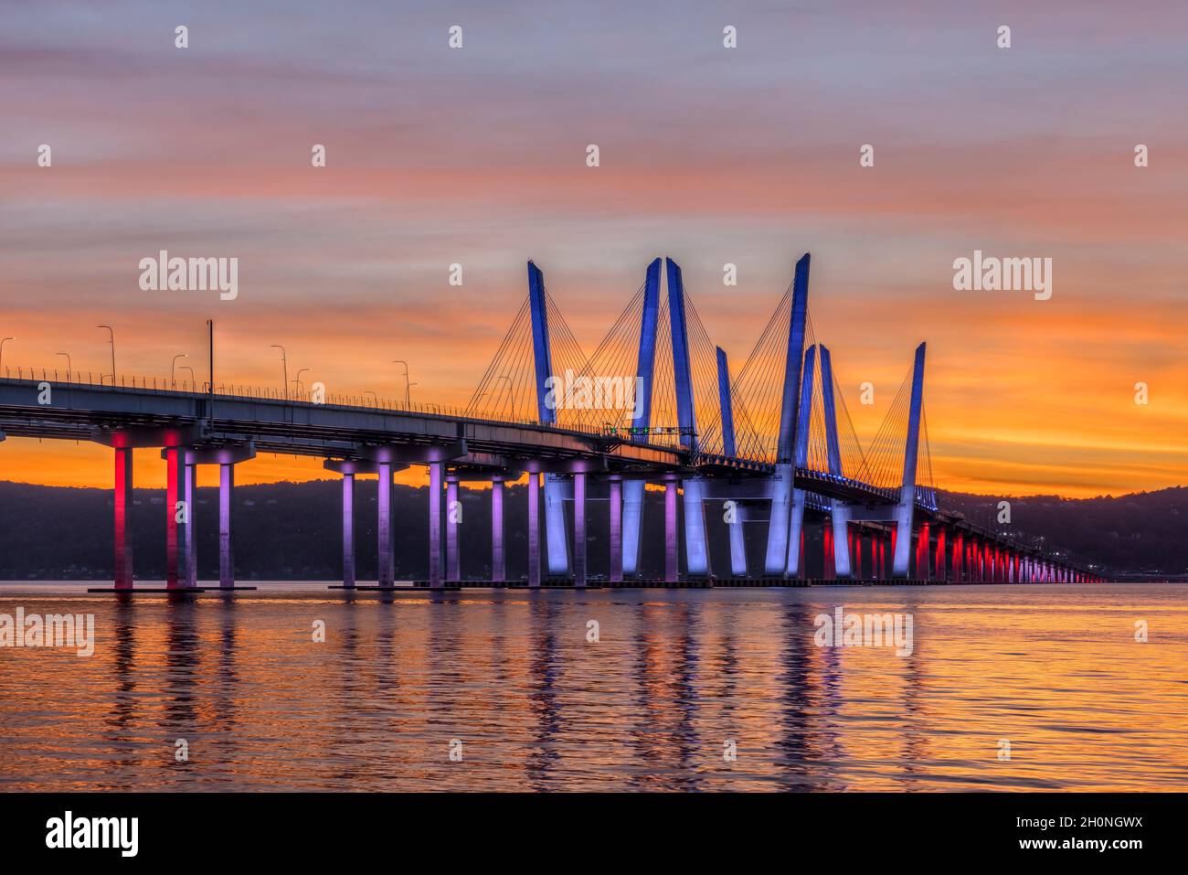 El Puente del Gobernador Mario M. Cuomo, iluminado en rojo, blanco y azul en reconocimiento al Día de Colón, abarca el río Hudson justo después de la puesta del sol. Foto de stock