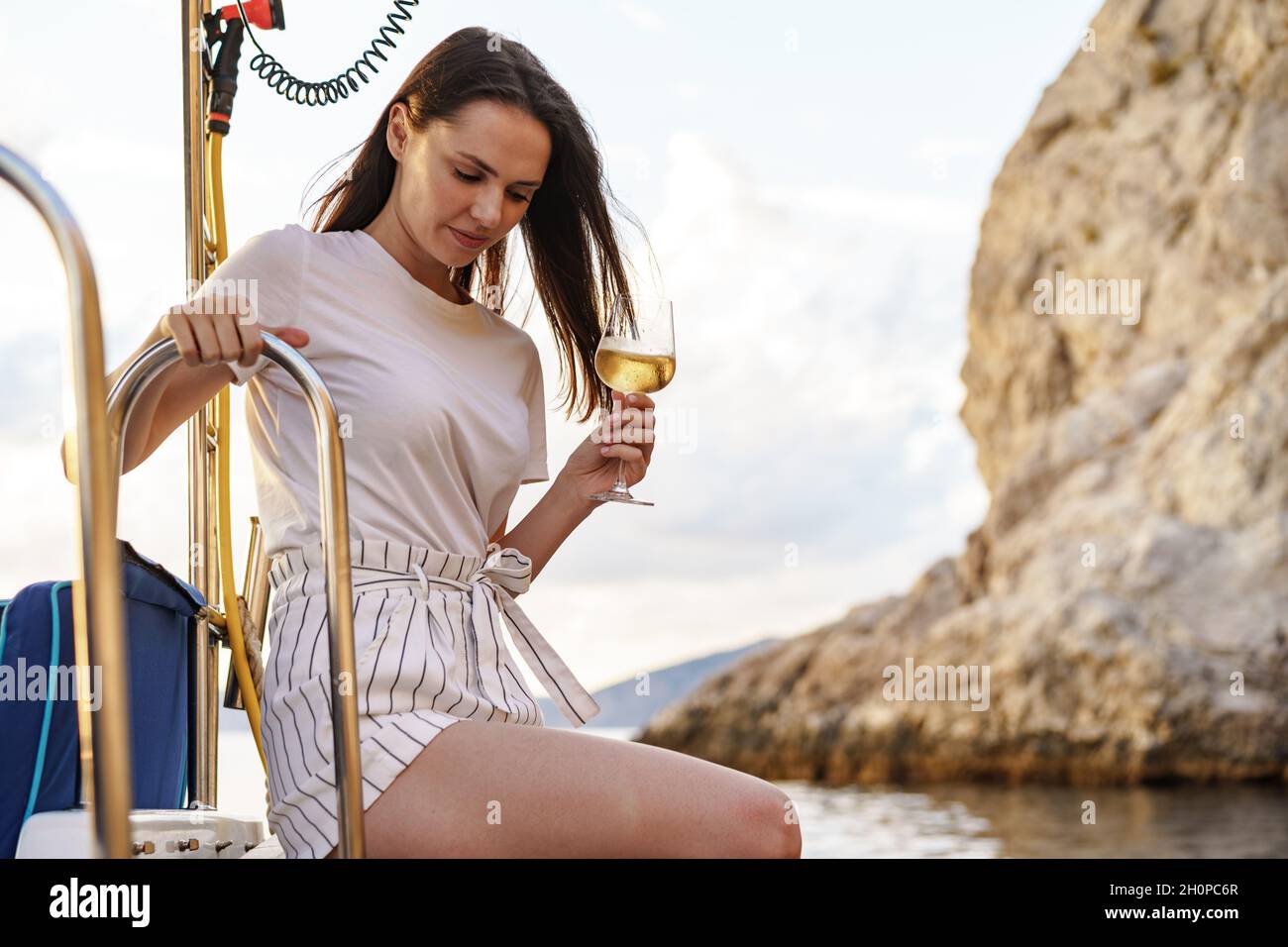 Mujer joven sosteniendo una copa de vino y sentada en la cubierta del velero Foto de stock
