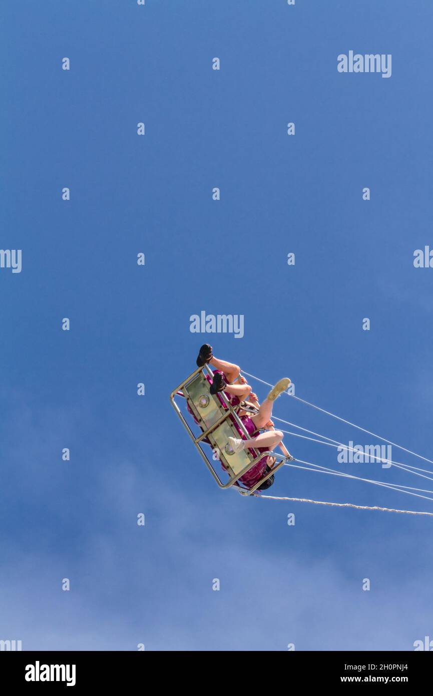Personas sentadas en una silla voladora Ride en un Funfair UK contra un cielo azul Foto de stock