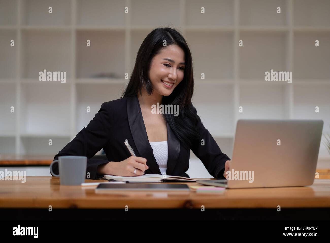 Mujer de negocios asiática que trabaja en un ordenador portátil durante la toma de notas en la oficina. Concepto de seminario web para reuniones en línea. Foto de stock