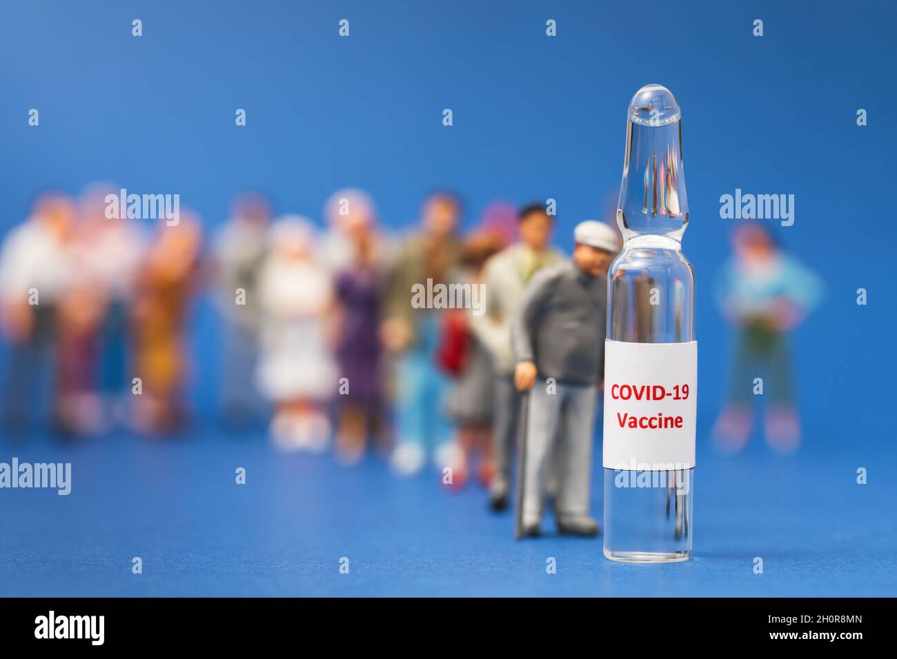 Los hombres de juguete y la ampolla con una vacuna sobre un fondo azul, concepto, las personas se alinean para la vacunación contra el coronavirus Foto de stock