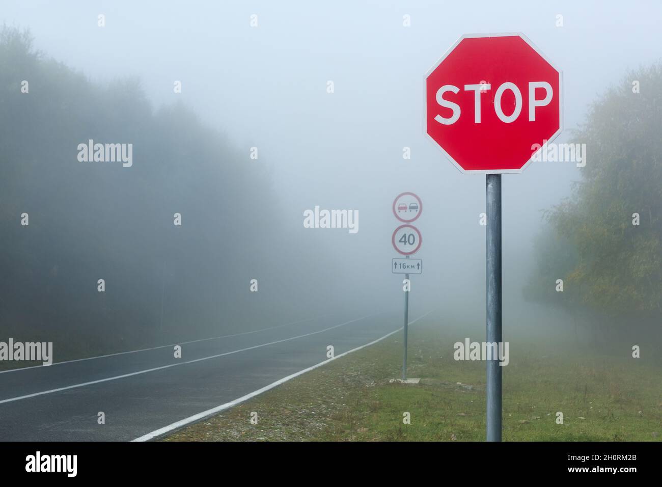 Niebla peligrosa en la carretera en las montañas, señal de límite de velocidad Foto de stock