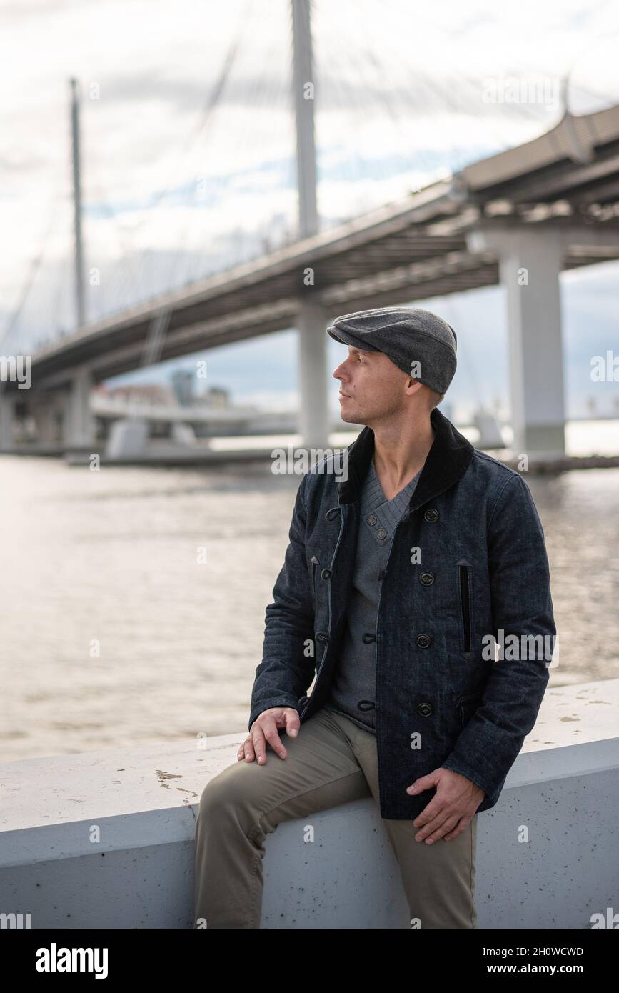 Un hombre en un abrigo y una gorra en el fondo del puente Fotografía de  stock - Alamy