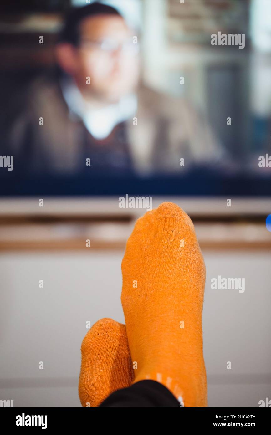Piernas en calcetines naranja contra el fondo de una pantalla de televisión borrosa - ocio por la noche viendo una película en casa Foto de stock